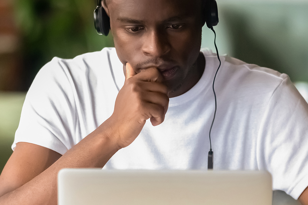 Transferência Graduação: Estudante africano focado usa fones de ouvido estudando on-line, faça exercícios usando laptop, assistindo a vídeos, aprendendo idiomas