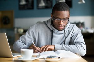 Segunda graduação: afro-americano em óculos fazendo anotações anotando informações do livro no café se preparando para teste ou exame